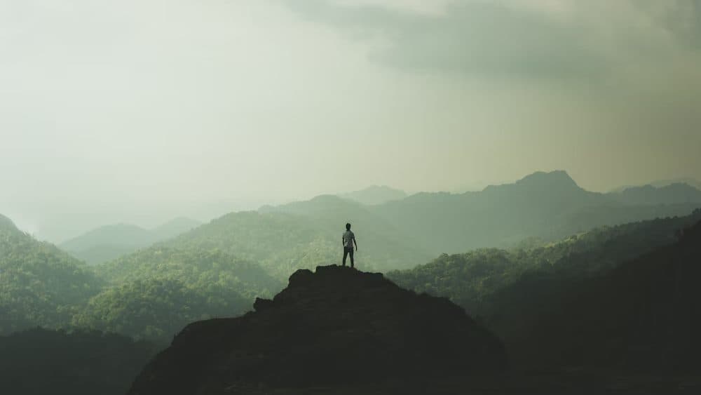 A lone figure on a rocky summit above misty hills